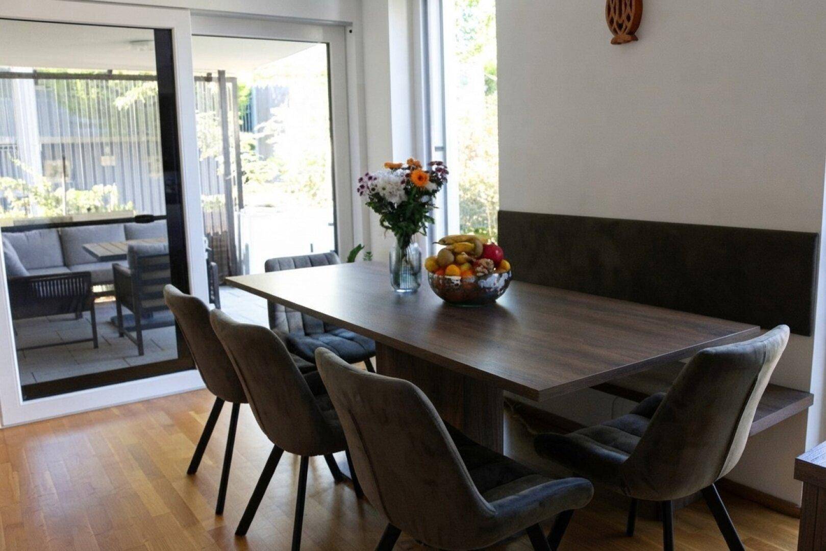 Heller Essbereich mit Holztisch, bequemen Stühlen und Zugang zur Terrasse.