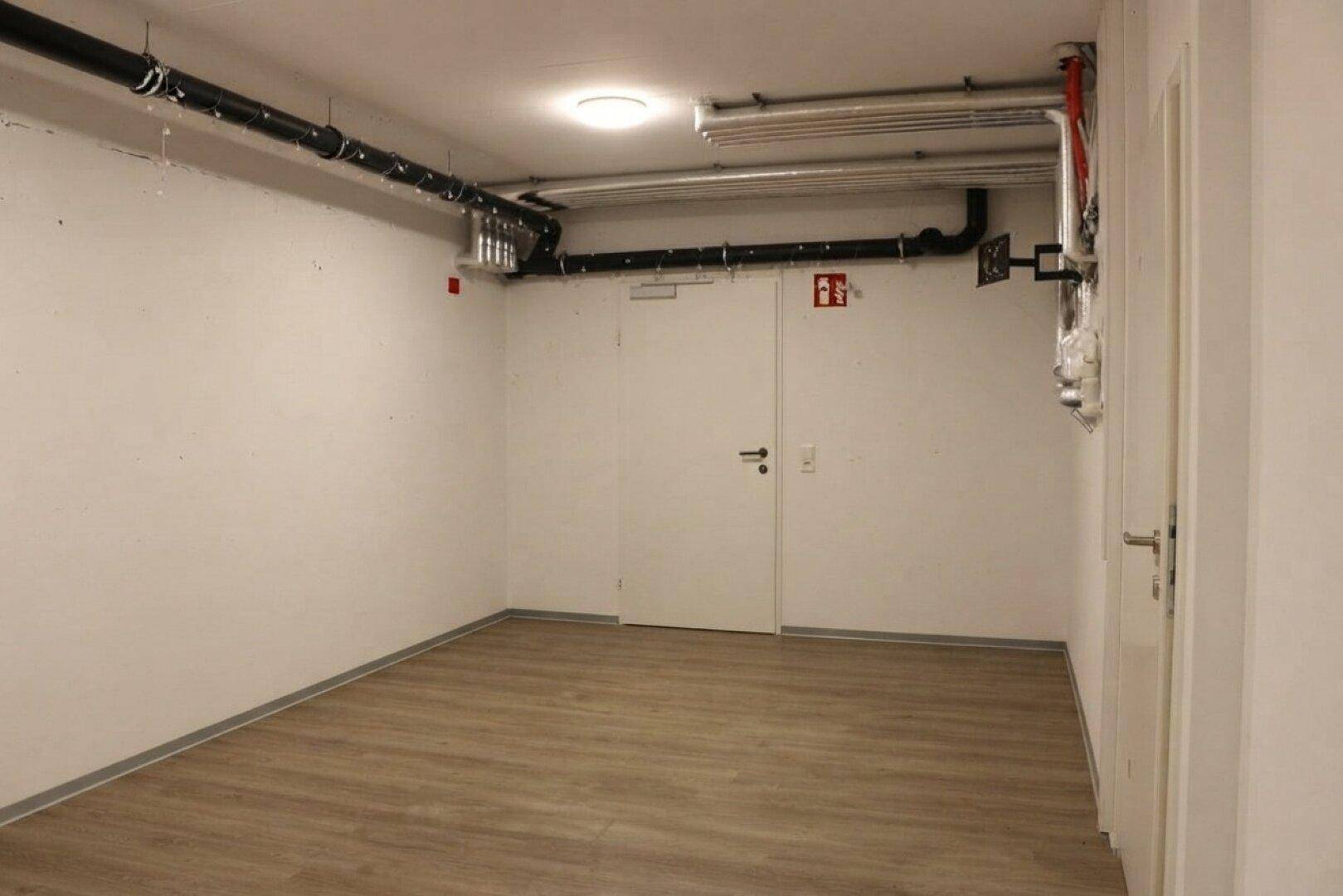 Geräumiger Kellerraum mit Laminatboden und sichtbaren Versorgungsleitungen.