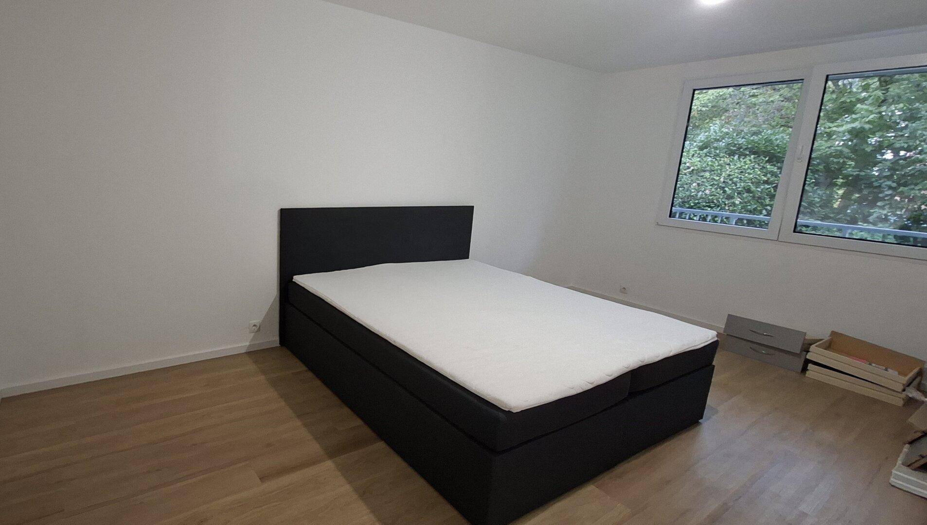 Schlafzimmer mit einem Doppelbett, Holzboden und einem großen Fenster, das viel Tageslicht hereinlässt.
