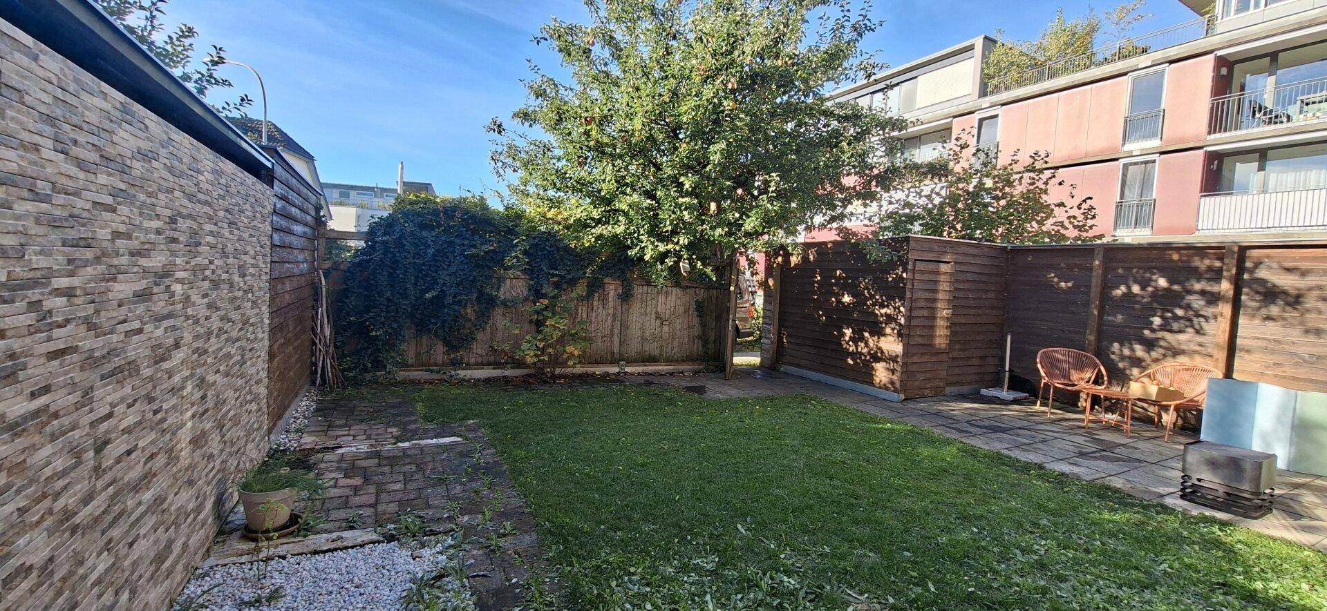 Gepflegter Gartenbereich mit Rasenfläche, Sitzgelegenheiten und umzäunt von Holzzäunen und einer Steinmauer.