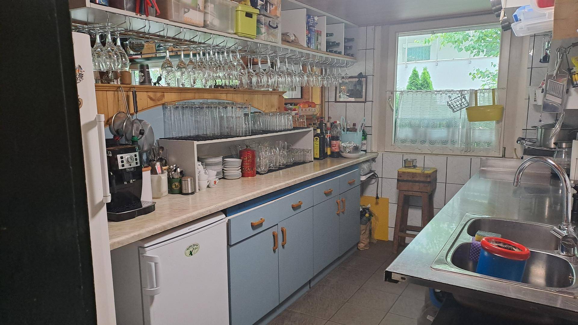 Funktionale Küche mit hellblauen Schränken, Edelstahlspüle und vielen Gläsern, ideal für den gewerblichen Gebrauch.