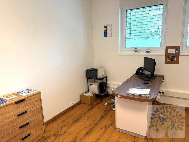Funktionales Büro mit Schreibtisch, Drucker und Laminatboden, gut beleuchtet durch ein großes Fenster.