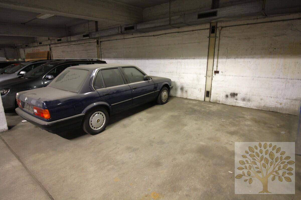 Stellplatz in einer Tiefgarage mit Betonwänden und einem älteren Fahrzeug, beleuchtet von Deckenlampen.