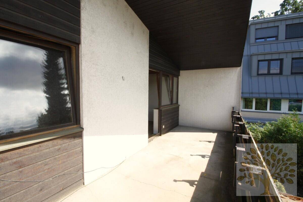 Schlichter Balkon mit Betonboden und Blick auf die umliegenden Gebäude und Bäume.