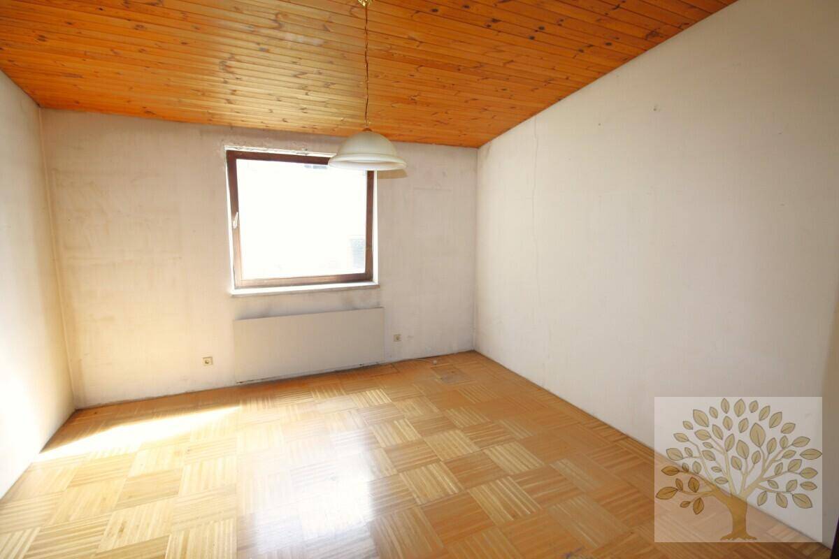 Gemütliches Zimmer mit Holzparkett, Holzdecke und einem Fenster, das Tageslicht hereinlässt.