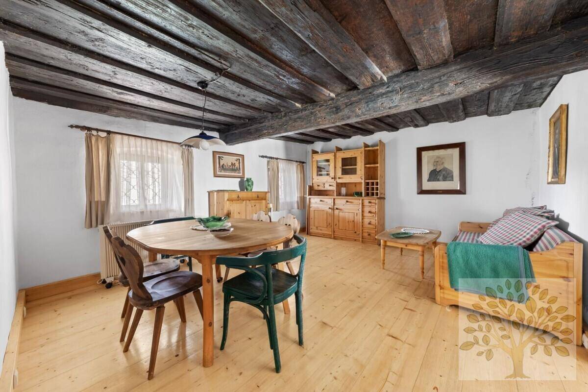 Rustikaler Wohn-Essbereich mit dunkler Holzbalkendecke, hellem Holzboden und traditionellen Holzmöbeln.