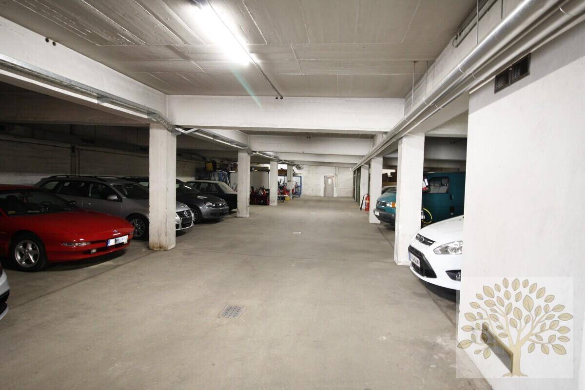 Weitläufige Tiefgarage mit vielen Stellplätzen, gekennzeichnet durch Betonwände und Deckenbalken.