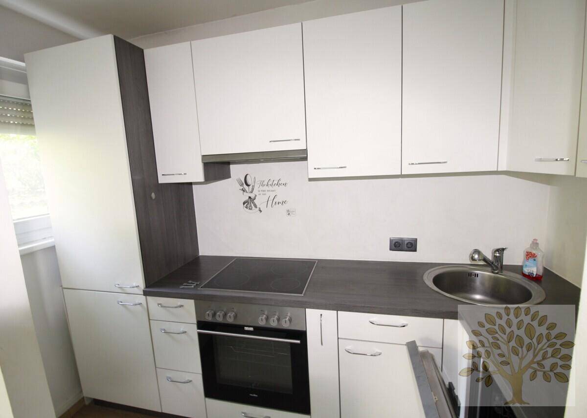 Funktionale Küche mit weißen Schränken, dunkler Arbeitsplatte, integriertem Backofen und Induktionskochfeld.