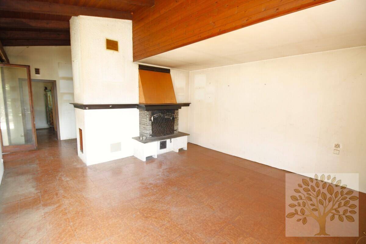 Geräumiges Wohnzimmer mit Kamin, Holzbalkendecke und einem markanten braunen Boden.
