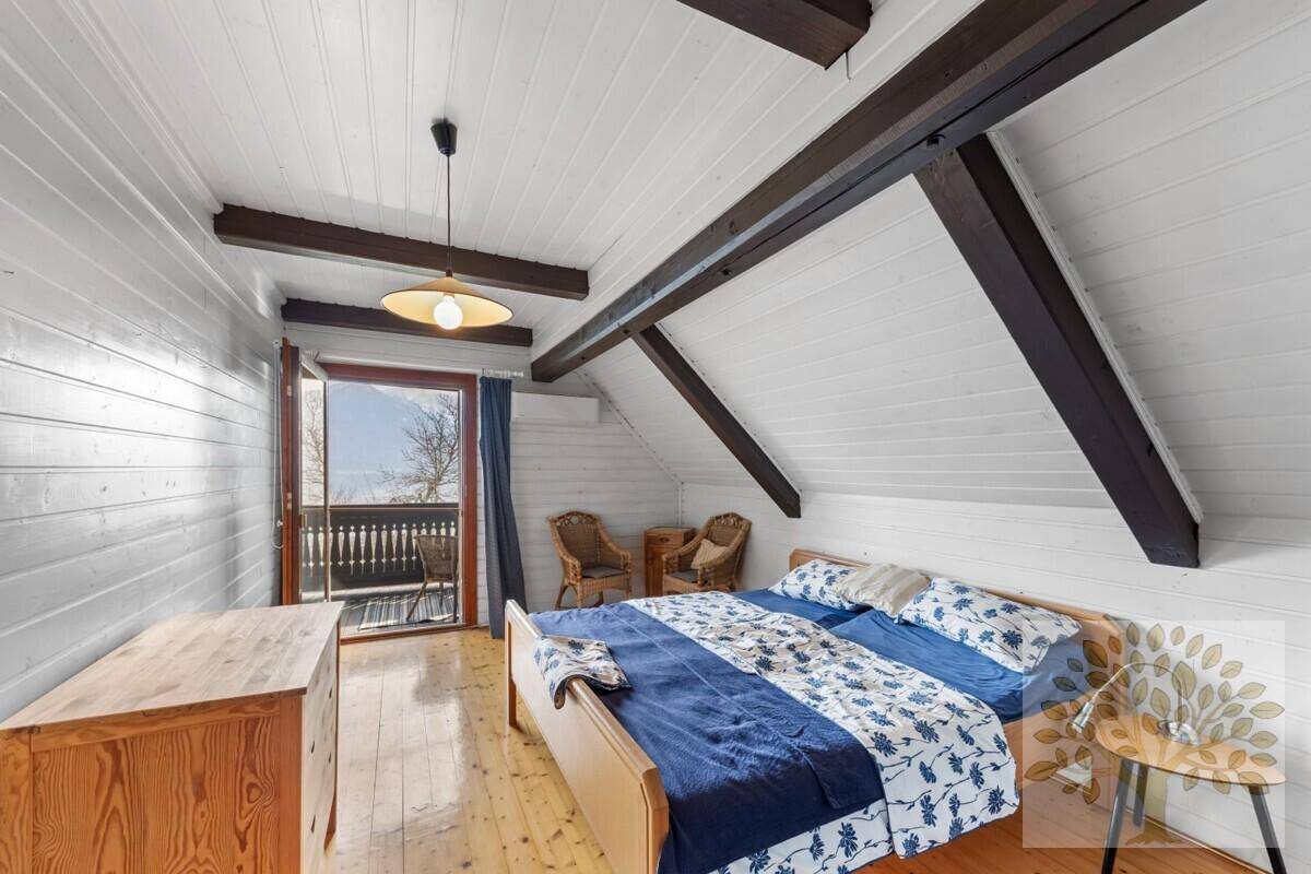 Gemütliches Schlafzimmer im Dachgeschoss mit sichtbaren Holzbalken, Holzboden und direktem Zugang zu einem Balkon.