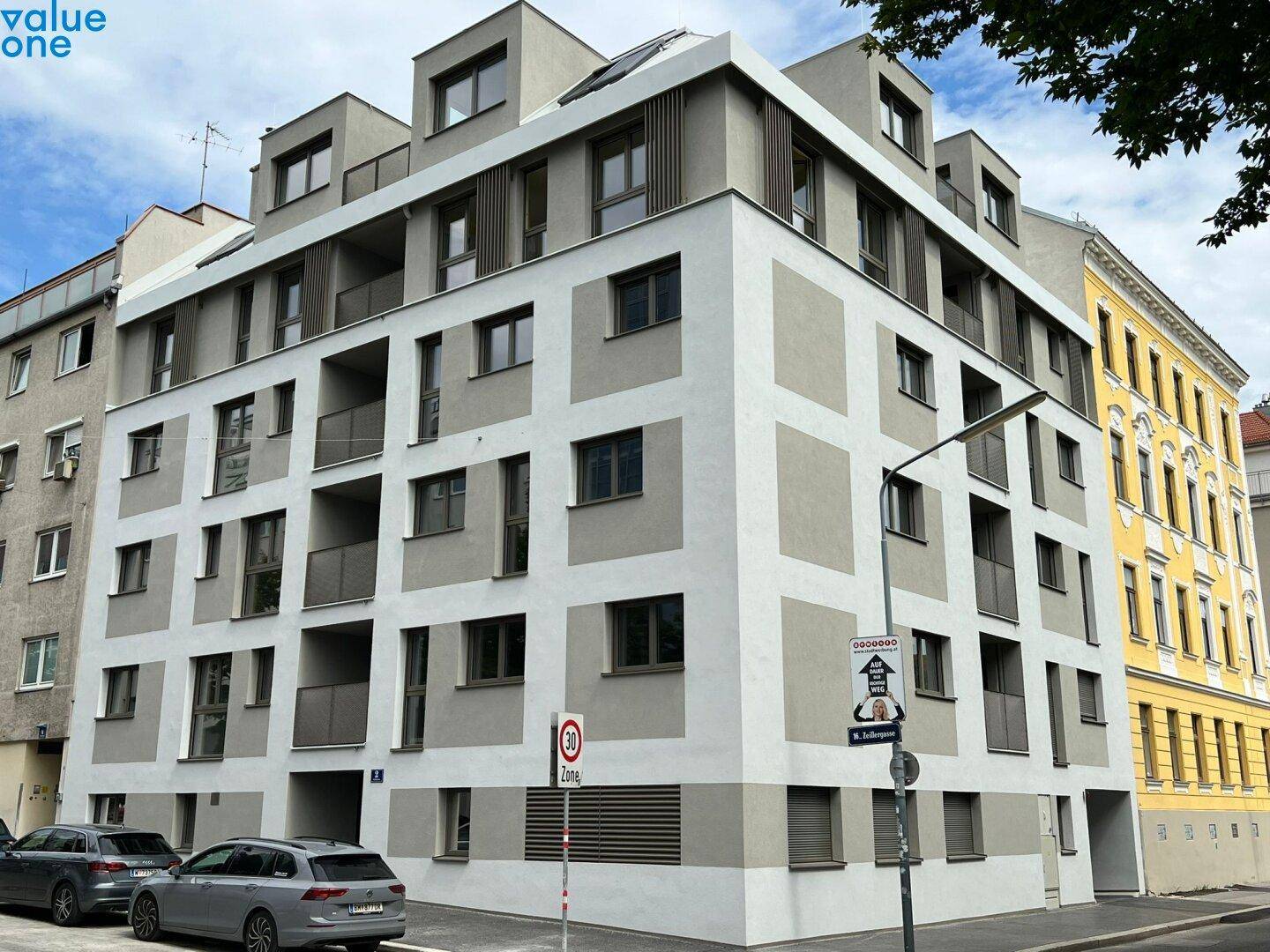 Modernes Wohngebäude mit grauer und weißer Fassade an einer Straßenecke im Tageslicht.