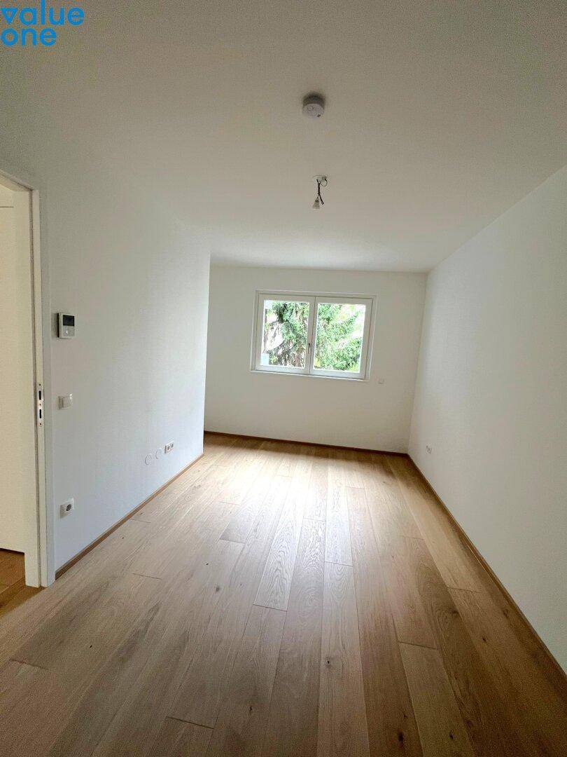 Heller, leerer Raum mit Holzboden und Fenster mit Blick ins Grüne, ideal als Schlaf- oder Arbeitszimmer.