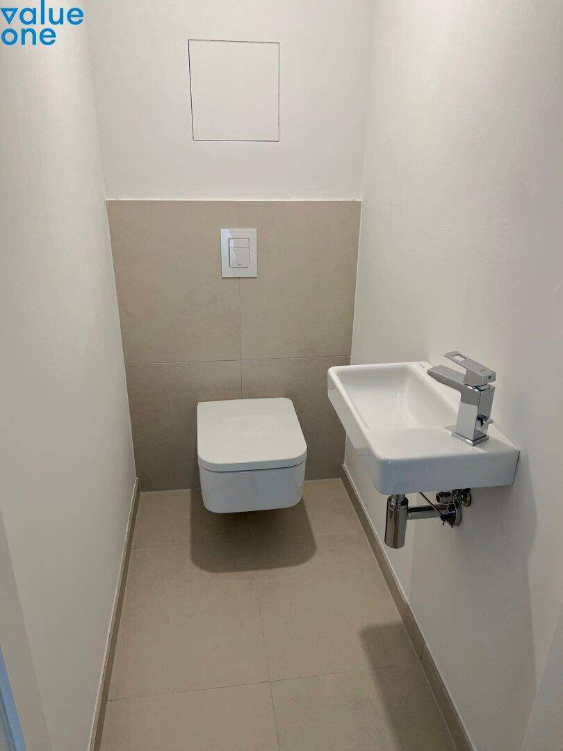Modernes Gäste-WC mit wandhängender Toilette, kleinem Waschbecken und hellen Fliesen.