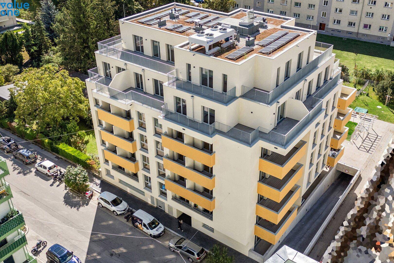 Modernes Mehrfamilienhaus mit zahlreichen Balkonen, Solaranlagen auf dem Dach und umliegender Grünfläche.