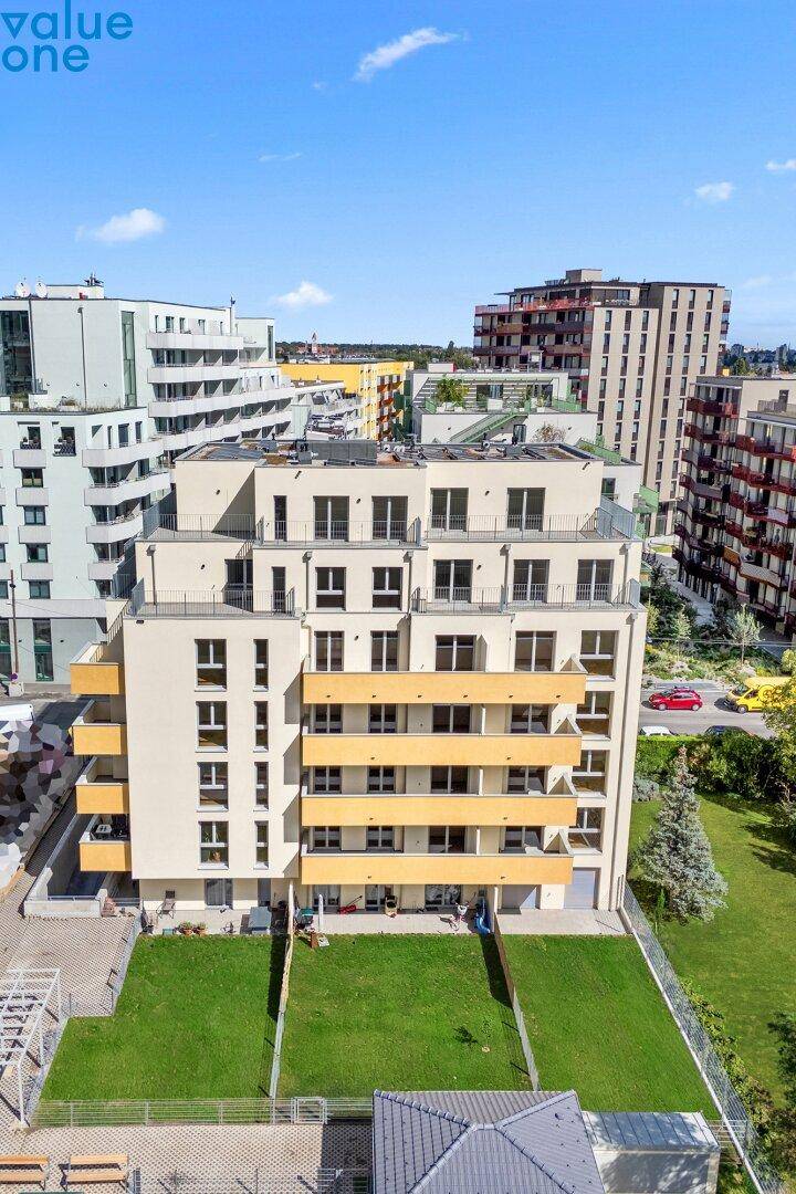 Rückansicht eines modernen Wohngebäudes mit gepflegter Rasenfläche und weiteren Neubauten im Hintergrund.