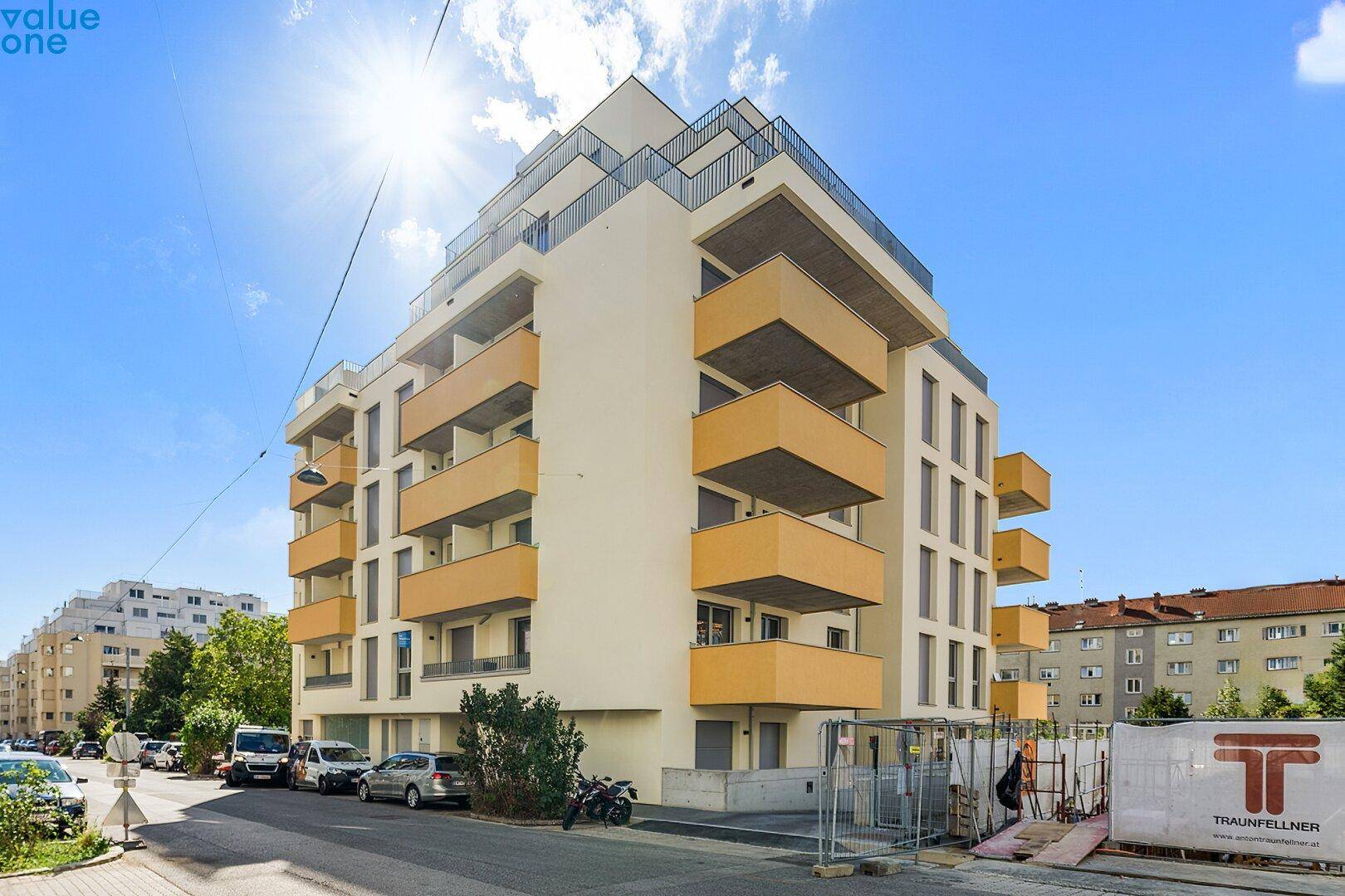 Modernes Wohngebäude mit markanten Balkonen und heller Fassade unter strahlend blauem Himmel.