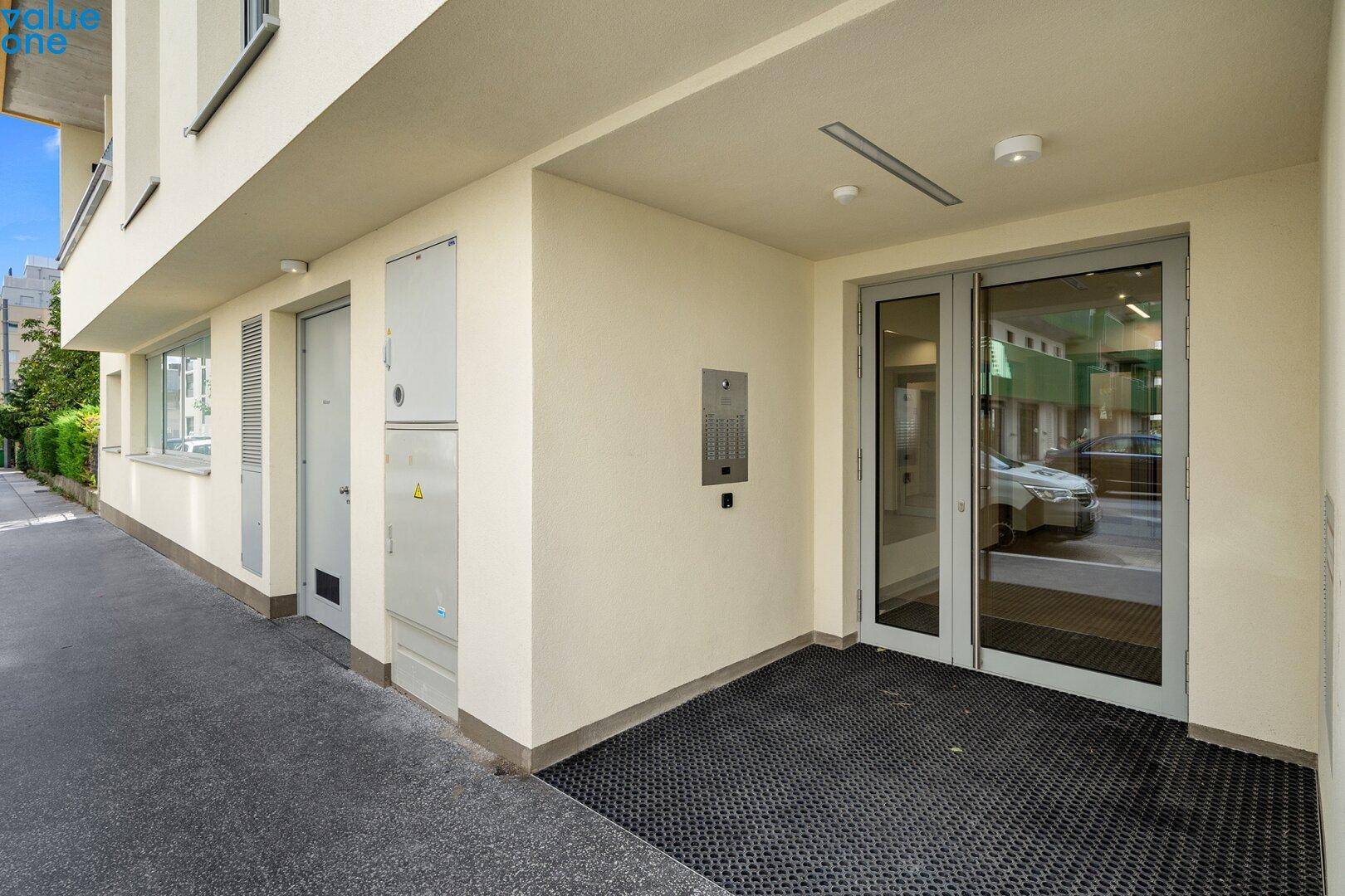 Eingangsbereich eines modernen Wohnhauses mit Glastüren und Gegensprechanlage.