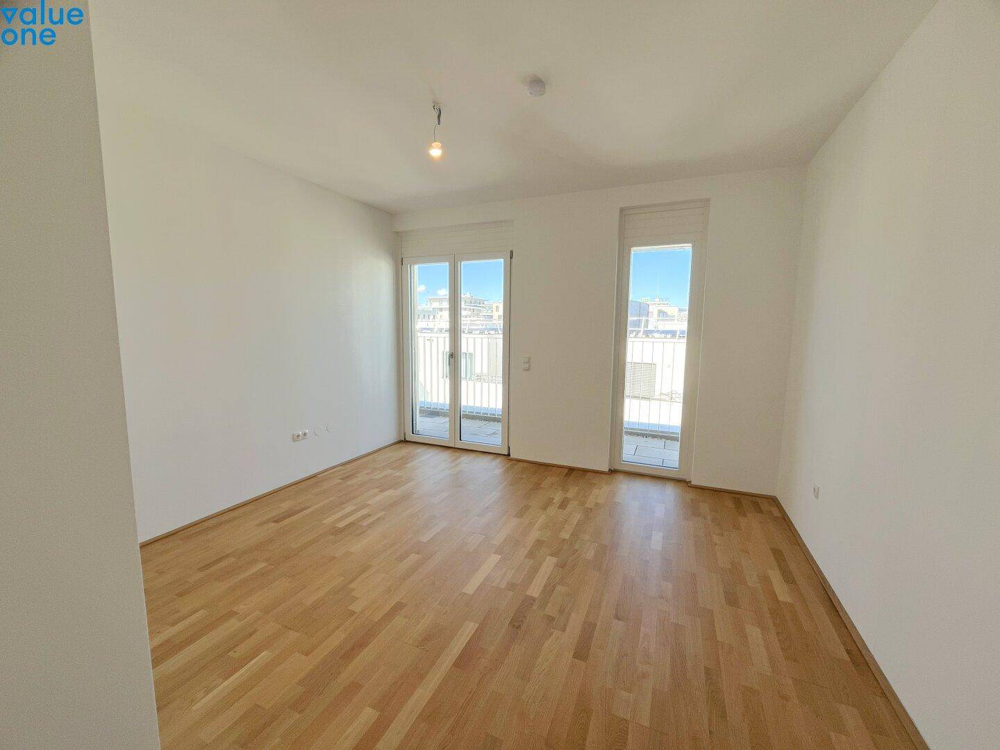 Geräumiges Schlafzimmer mit Parkettboden und zwei Fenstern mit Blick nach draußen.