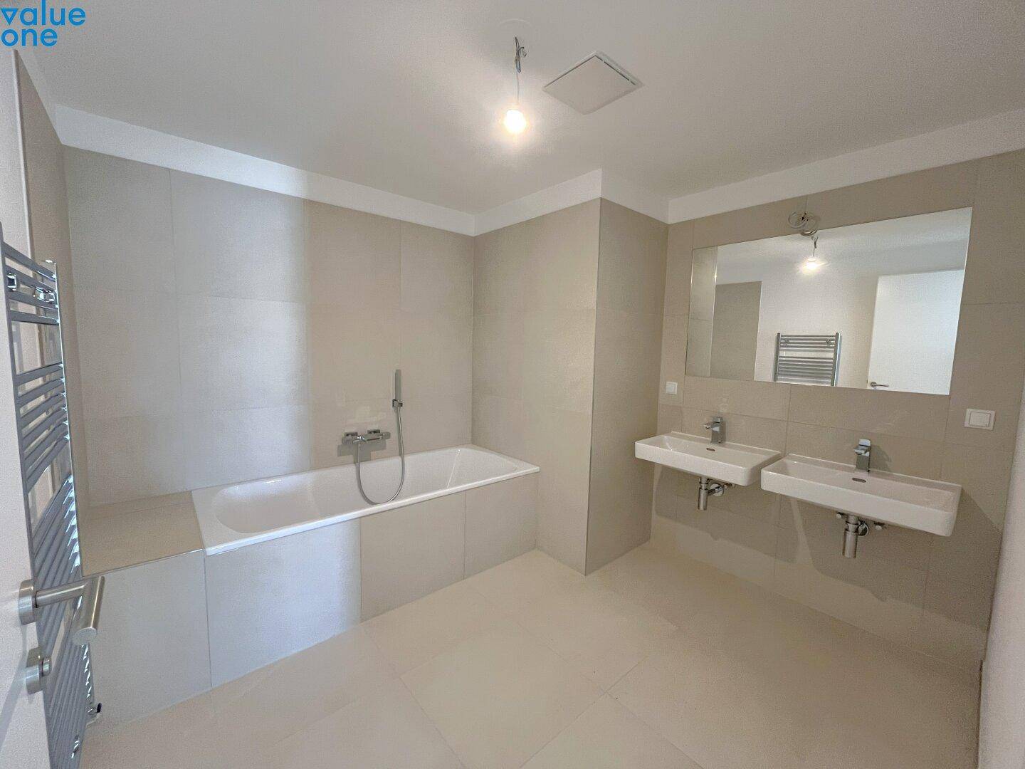 Helles Badezimmer mit Badewanne, zwei Waschbecken und großem Spiegel.