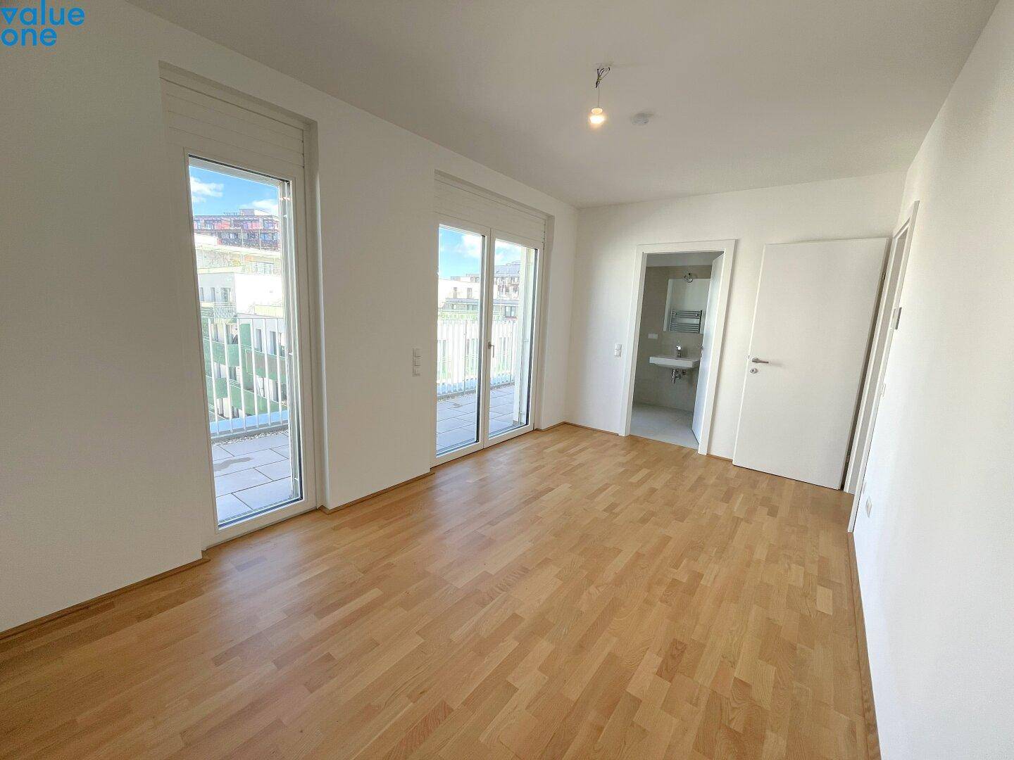 Leeres Schlafzimmer mit Parkettboden und direktem Zugang zu einem Badezimmer.