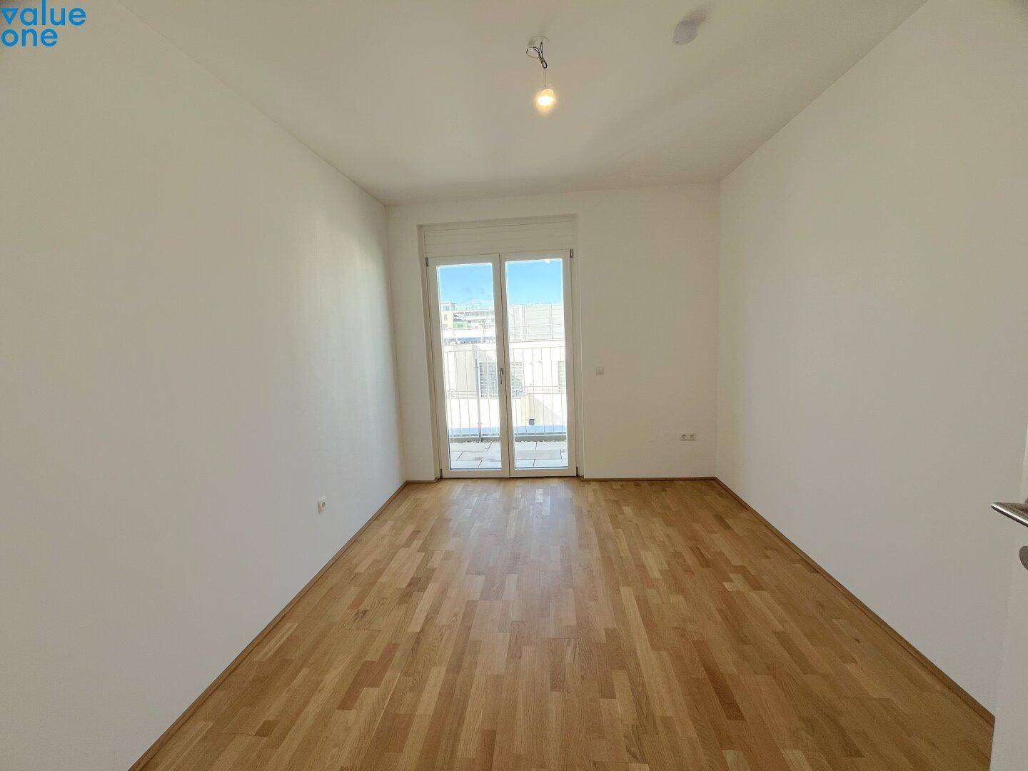 Helles Schlafzimmer mit Parkettboden und Zugang zu einem französischen Balkon.