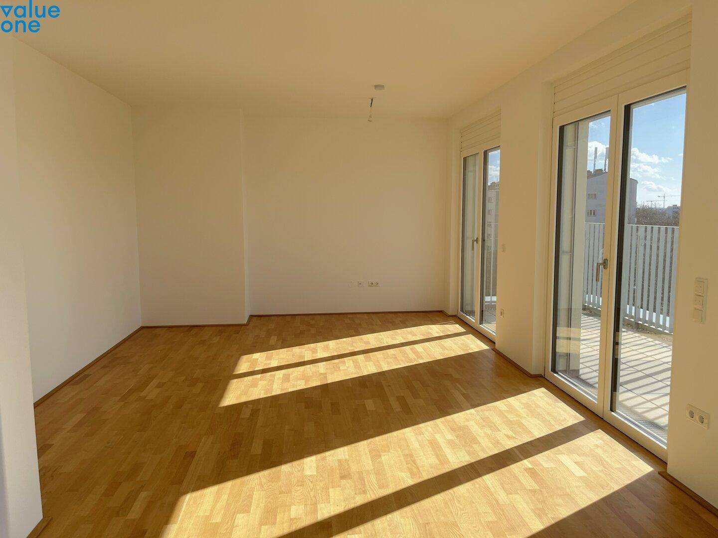 Geräumiges, leeres Wohnzimmer mit hellem Parkettboden und großen Fenstern zur Terrasse.