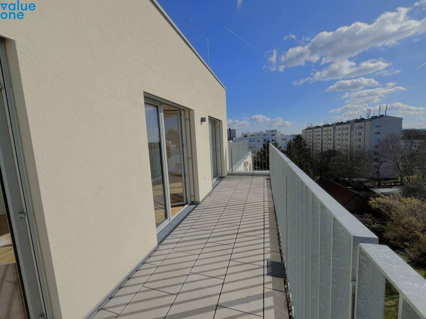Langer Balkon mit Fliesenboden und Blick auf die umliegenden Gebäude und Grünflächen.