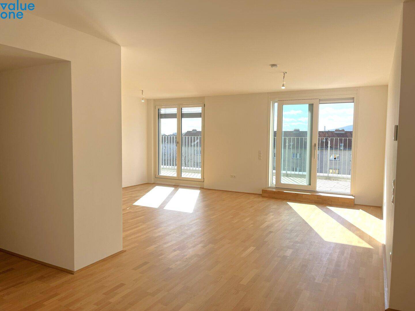Lichtdurchflutetes Wohnzimmer mit Holzboden und Zugang zu zwei Balkonen, bietet viel Helligkeit.