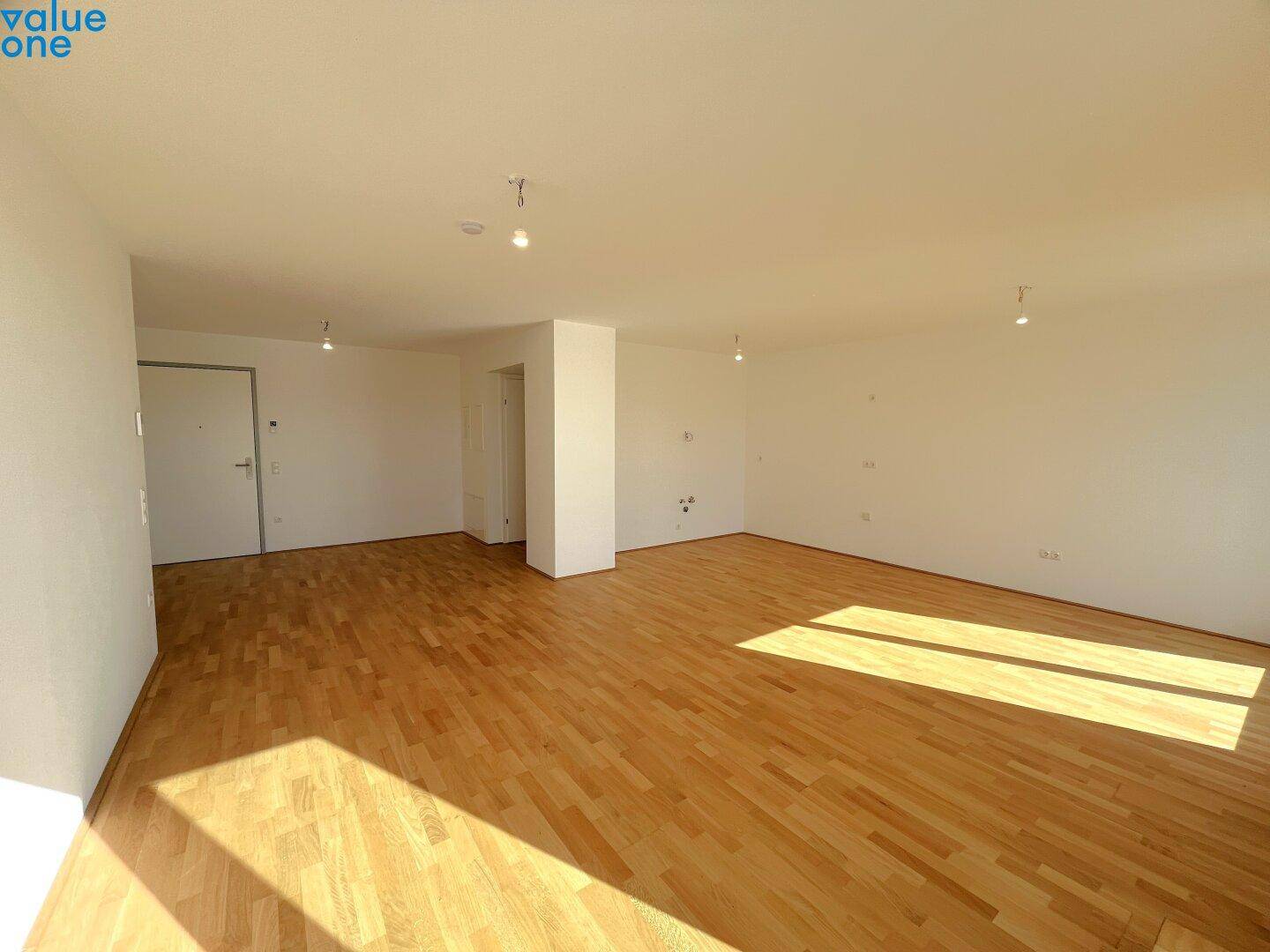 Geräumiges, leeres Wohnzimmer mit hellem Holzboden und viel Tageslicht, bereit zur individuellen Gestaltung.