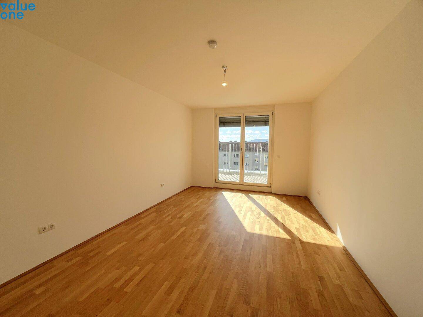 Helles Zimmer mit Holzboden und Zugang zum Balkon, bietet viel Tageslicht und frische Luft.