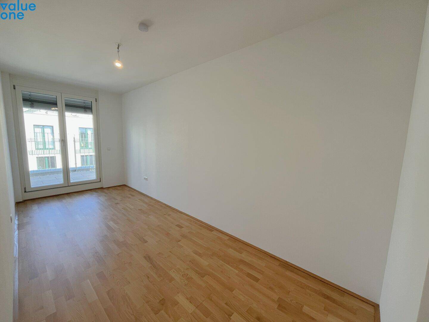 Geräumiges, helles Zimmer mit Holzboden und Balkonzugang, ideal als Schlaf- oder Arbeitszimmer.