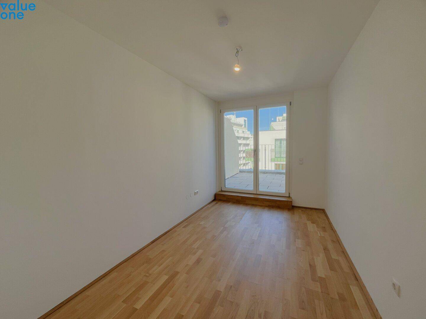 Helles Zimmer mit Holzboden und Zugang zum Balkon, bietet eine angenehme Wohnatmosphäre.