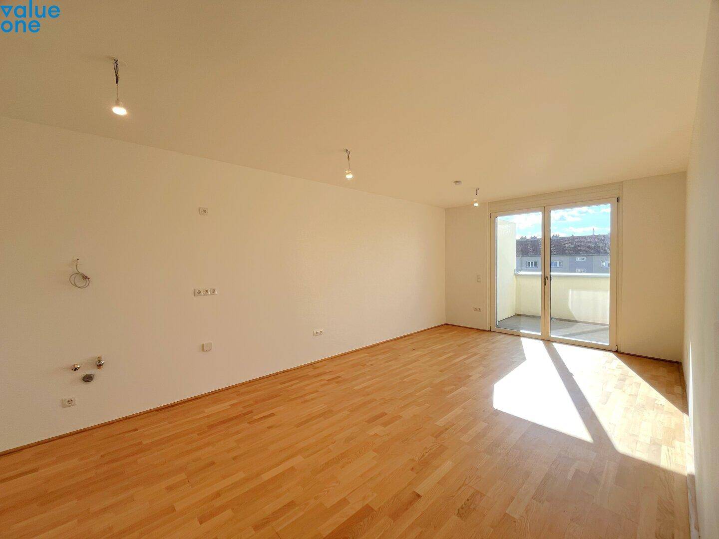 Geräumiger, unmöblierter Wohnbereich mit Parkettboden und großen Fenstern zum Balkon.