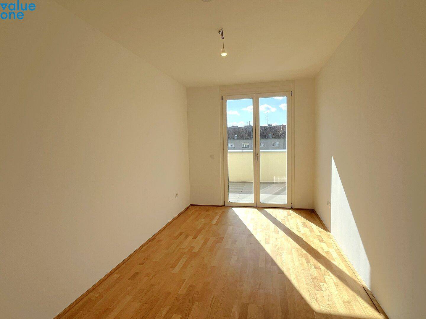 Unmöbliertes Zimmer mit Parkettboden und direktem Zugang zu einem sonnigen Balkon.