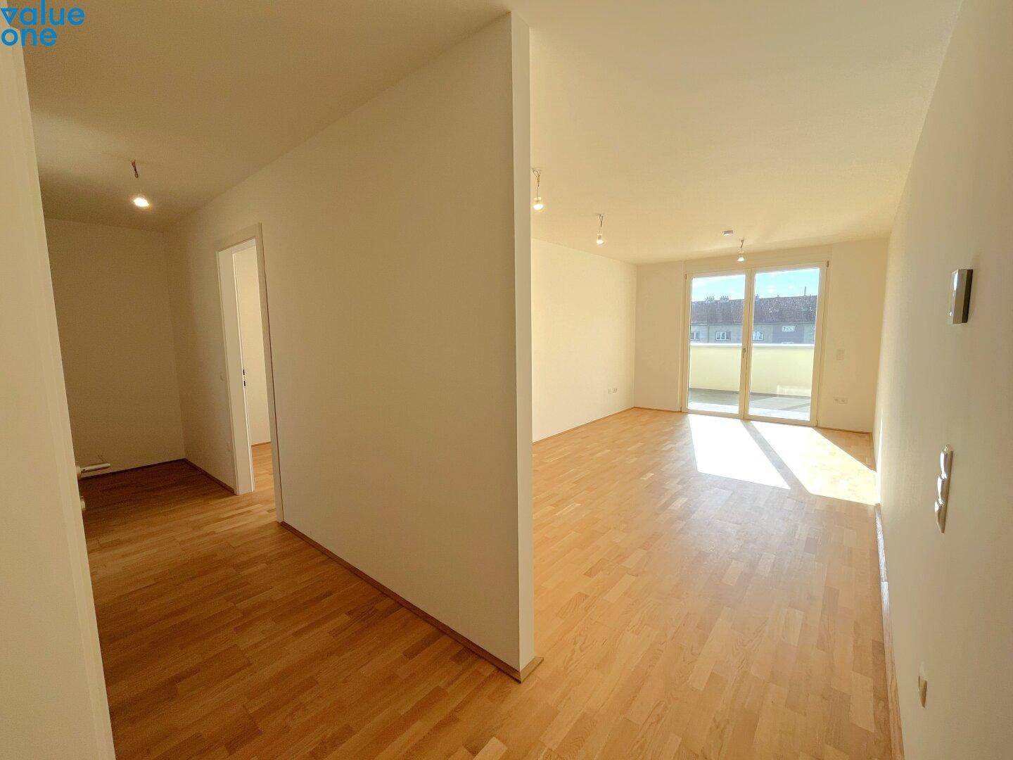 Geräumiger, leerer Wohnbereich mit Holzboden und Zugang zu einem Balkon.