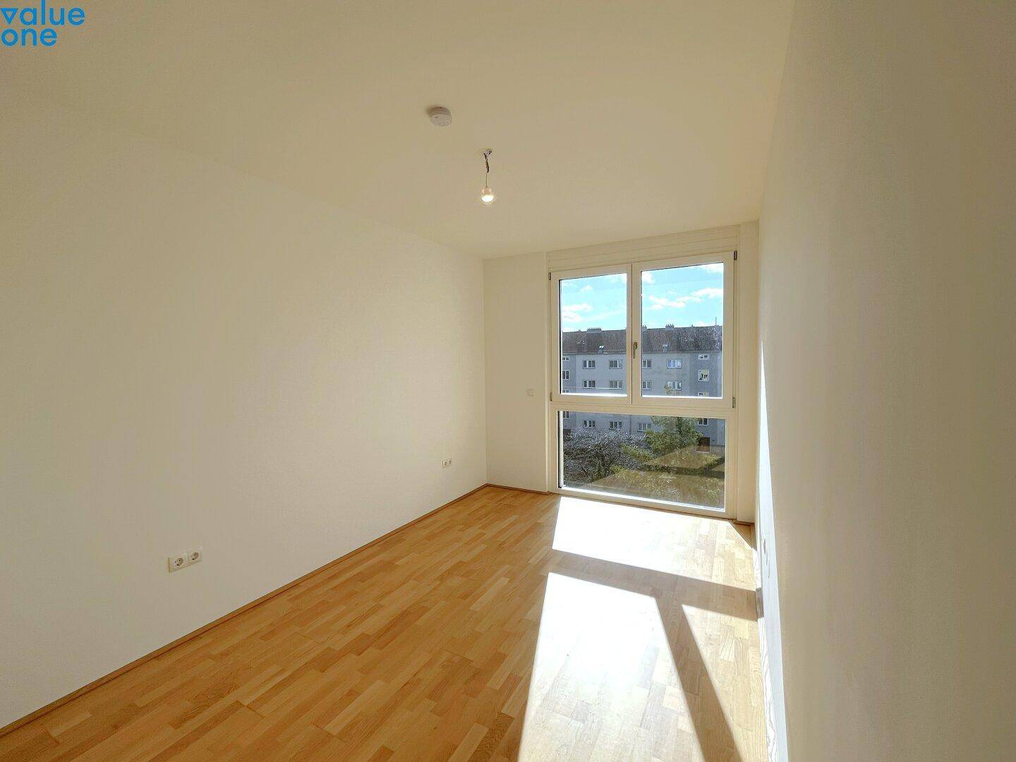 Geräumiges, helles Zimmer mit Holzboden und großem Fenster, ideal als Schlafzimmer.