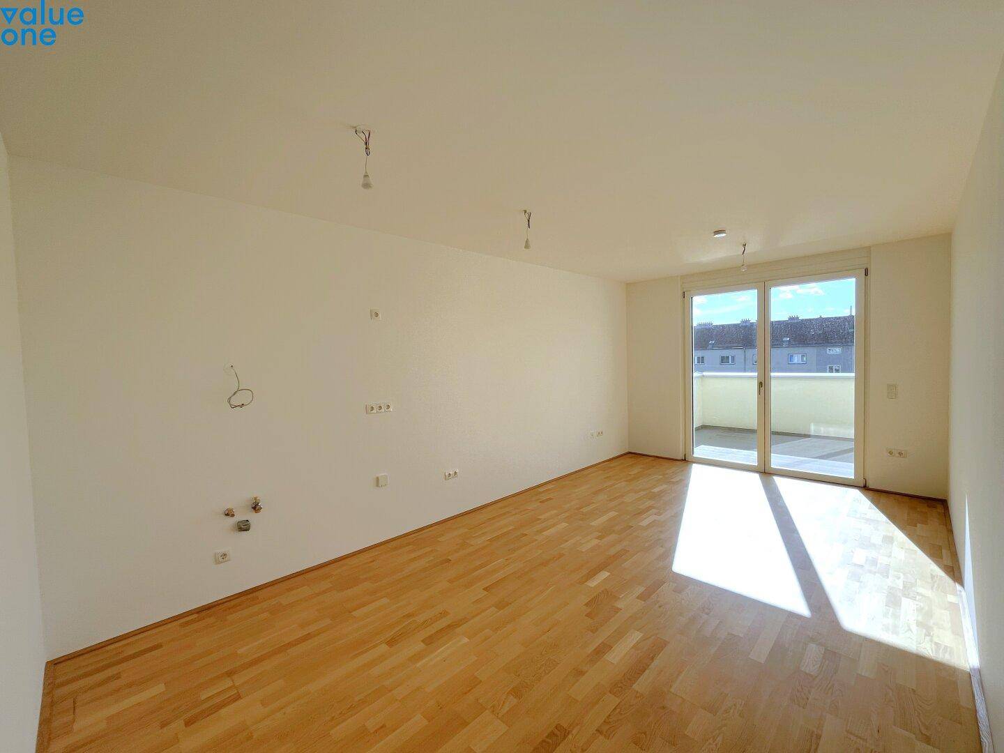 Helles, leeres Wohnzimmer mit Holzboden und großen Fenstern zum Balkon.