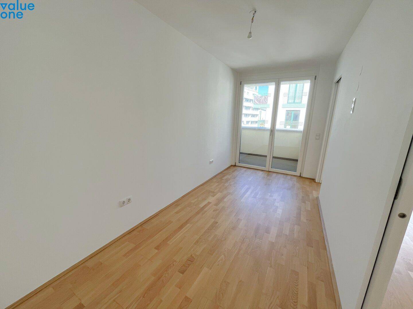 Leeres Zimmer mit Parkettboden und Zugang zu einem französischen Balkon.