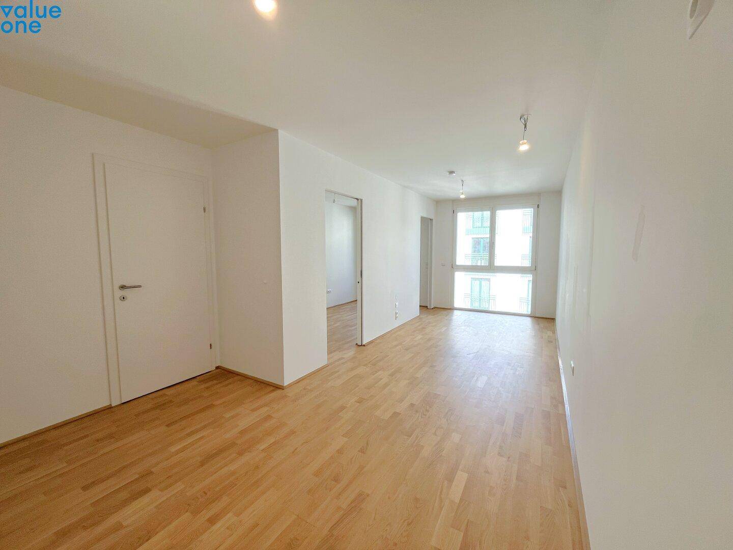 Heller Wohnraum mit Parkettboden und großen Fenstern, der einen offenen Übergang zu einem weiteren Zimmer bietet.