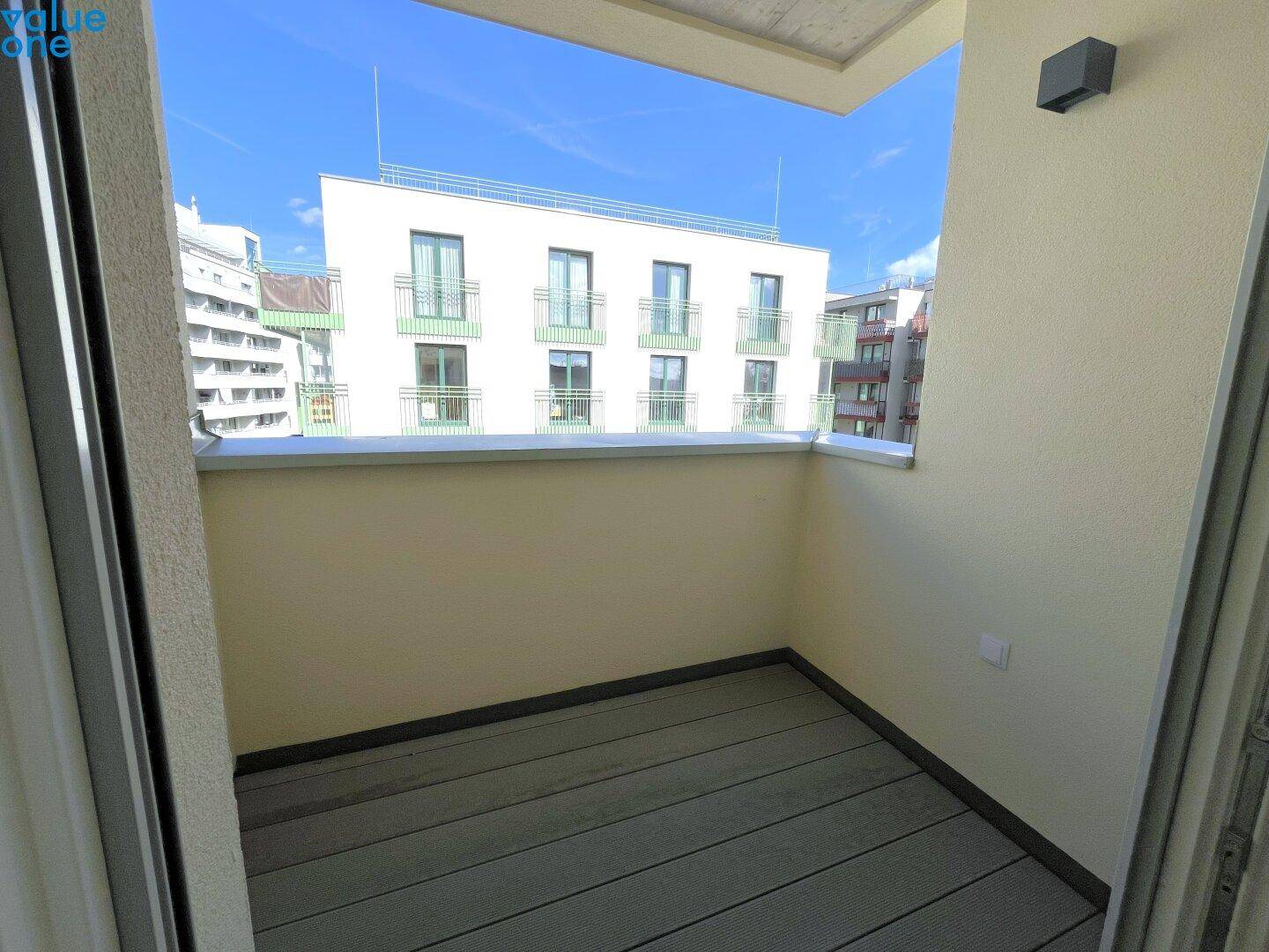 Heller, leerer Balkon mit Holzboden und Blick auf die moderne Architektur der Umgebung.