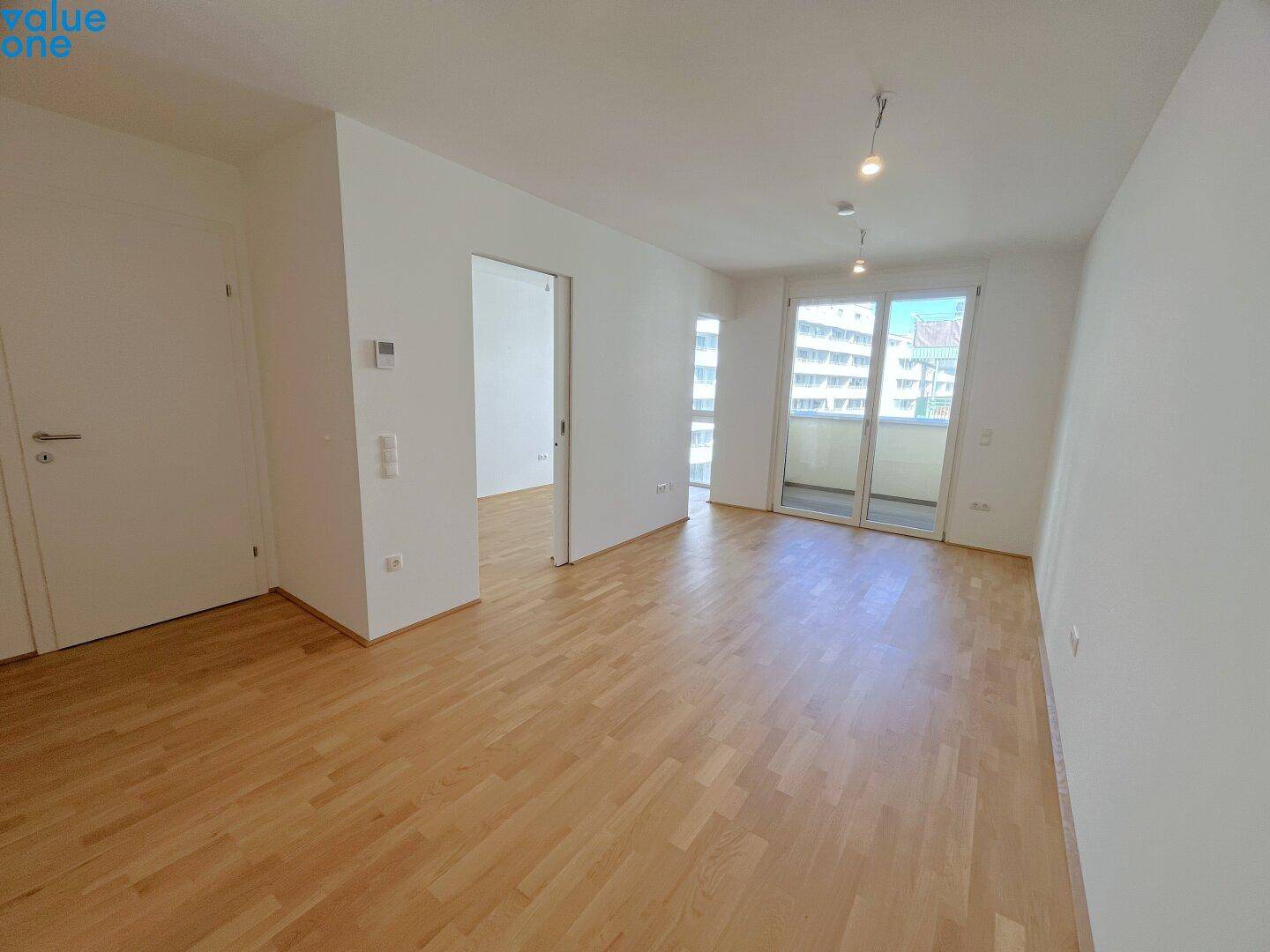 Heller Wohnbereich mit Holzboden und Zugang zu einem Balkon, bereit zur individuellen Gestaltung.