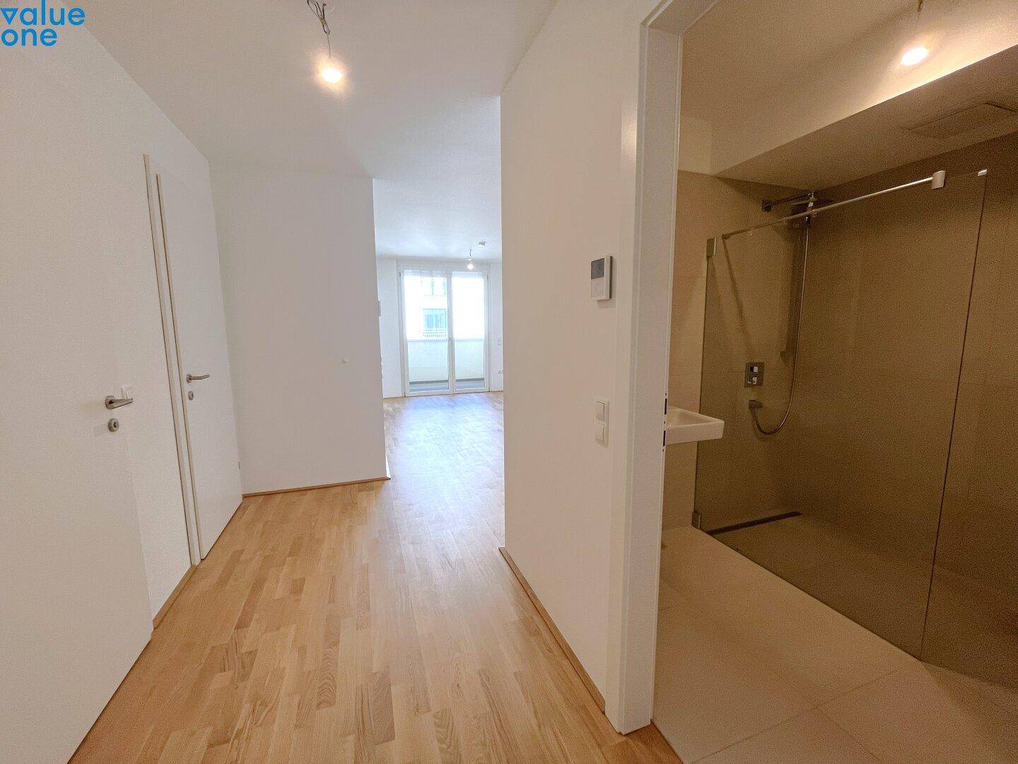 Flur mit Holzboden und Blick in ein modernes Badezimmer mit begehbarer Dusche.