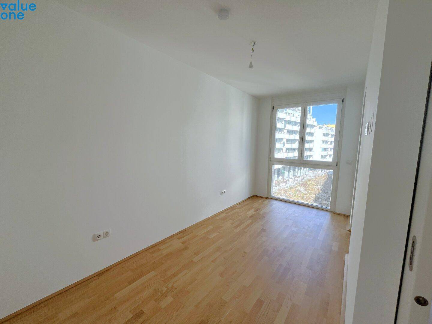 Leeres Schlafzimmer mit Holzboden und großem Fenster, das viel Tageslicht bietet.