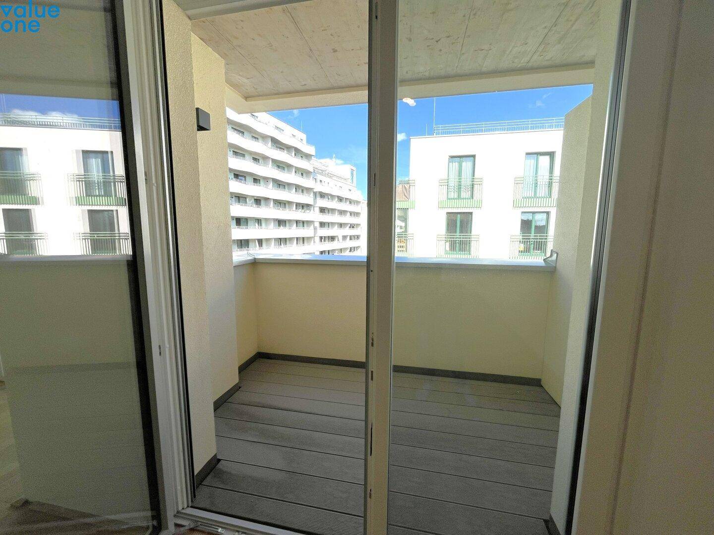 Leerer Balkon mit Holzdielenboden und Blick auf umliegende Gebäude.