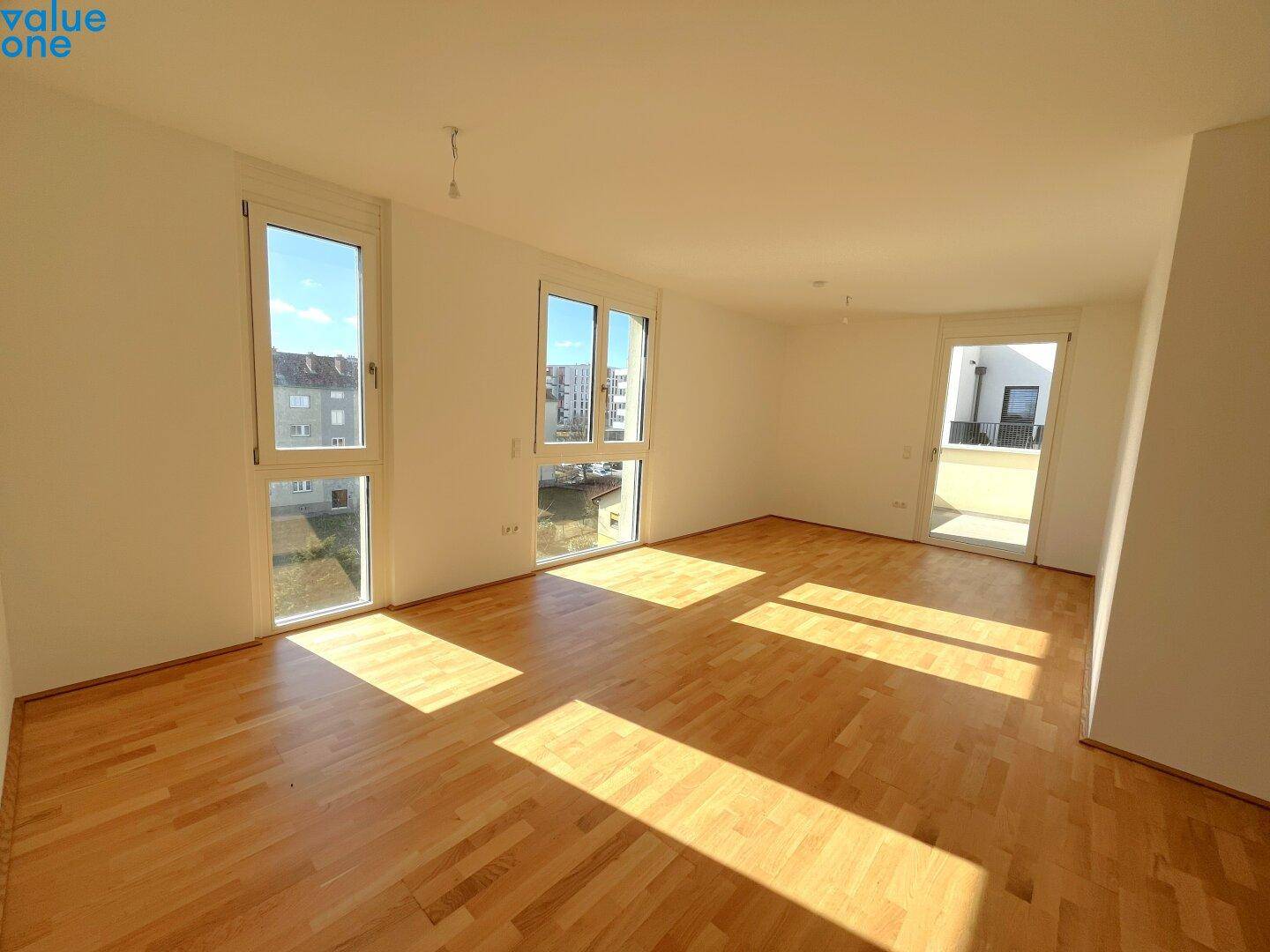 Lichtdurchfluteter Wohnraum mit Holzboden und großen Fenstern, die viel Sonne hereinlassen.