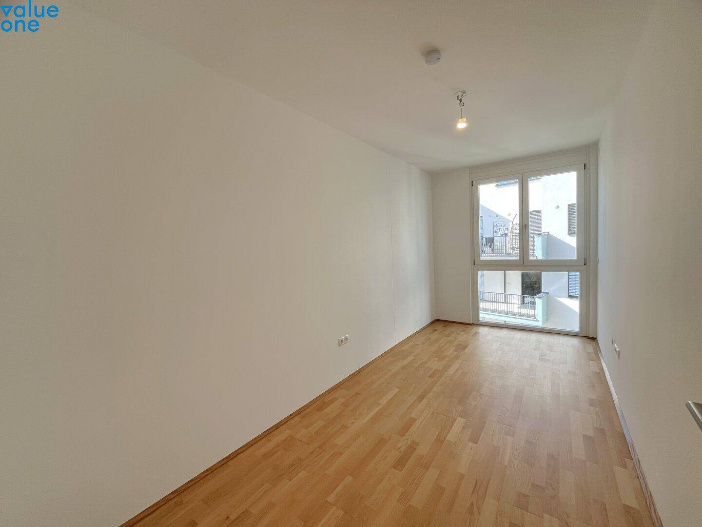 Leeres Schlafzimmer mit hellem Parkettboden und Zugang zu einem französischen Balkon.