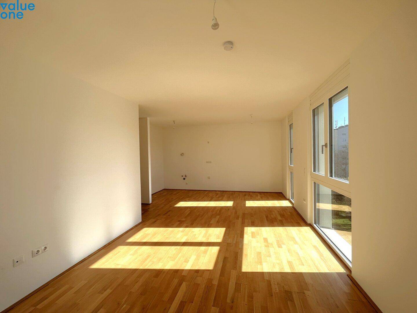 Geräumiger, heller Wohnraum mit Holzboden und großen Fenstern, die den Raum erhellen.