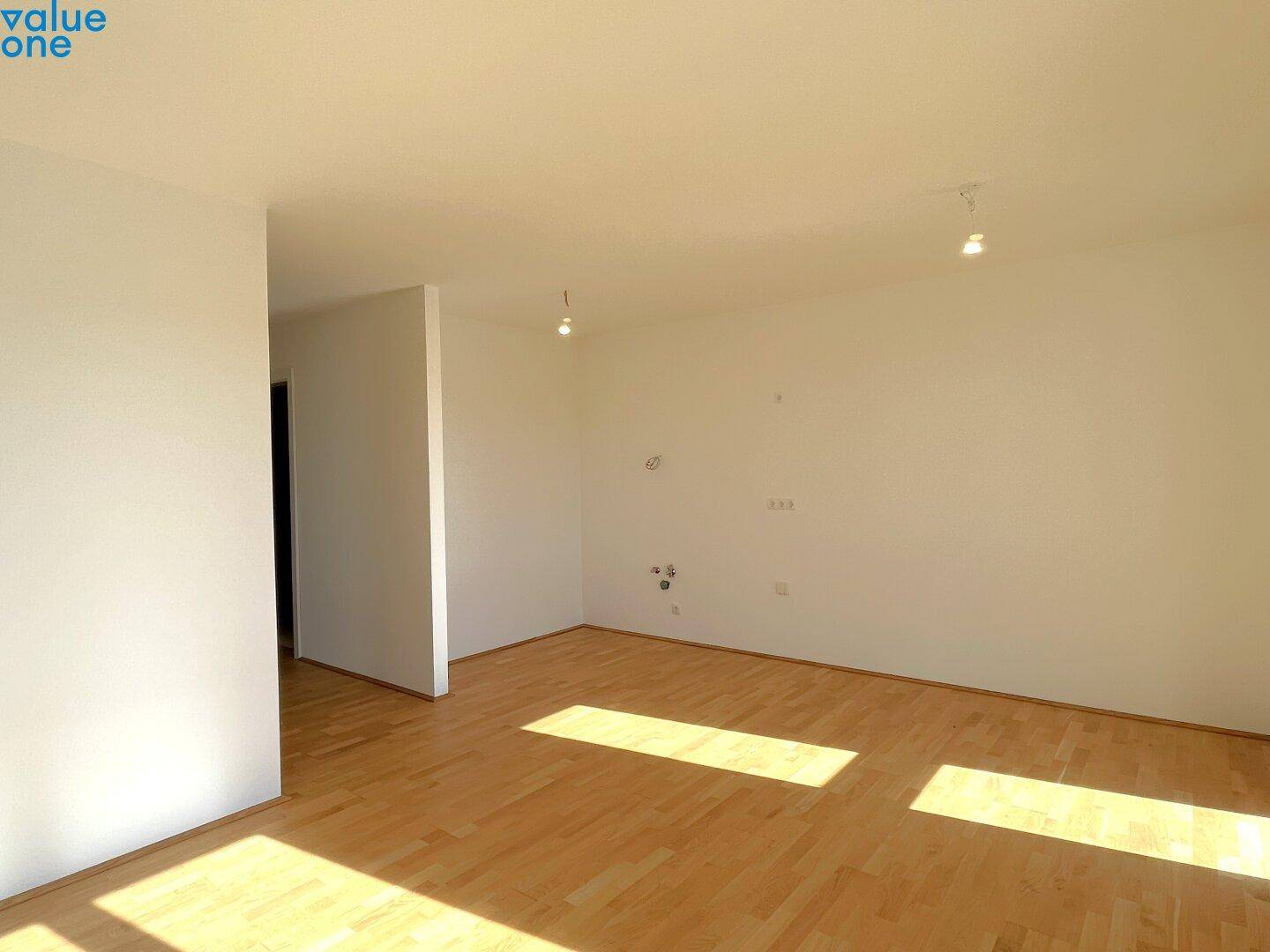 Geräumiger, leerer Wohnbereich mit Holzboden und viel natürlichem Licht durch große Fenster.