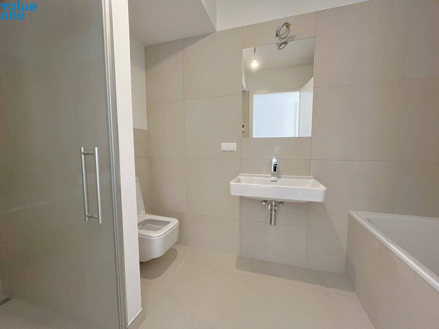 Unmöbliertes Badezimmer mit Dusche, Badewanne und modernen hellen Fliesen.
