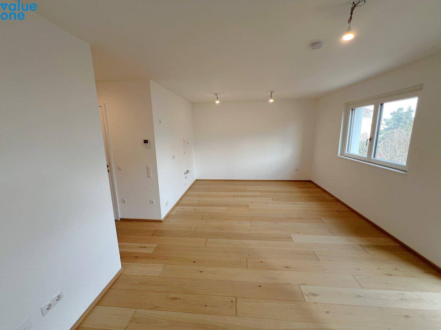 Heller und leerer Wohnbereich mit Holzboden und großem Fenster.